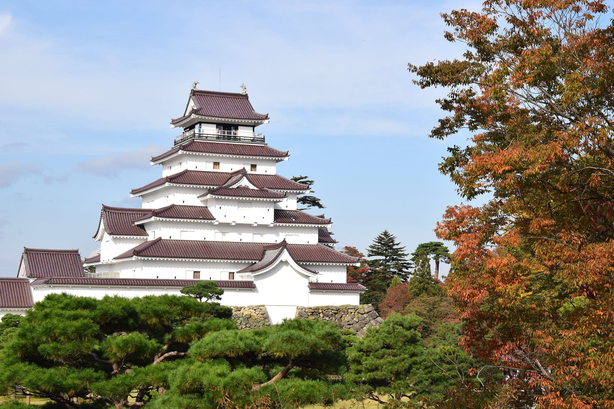 The red-tiled keep of Tsuruga Castle rises above pines and autumn maples in Aizu-Wakamatsu.