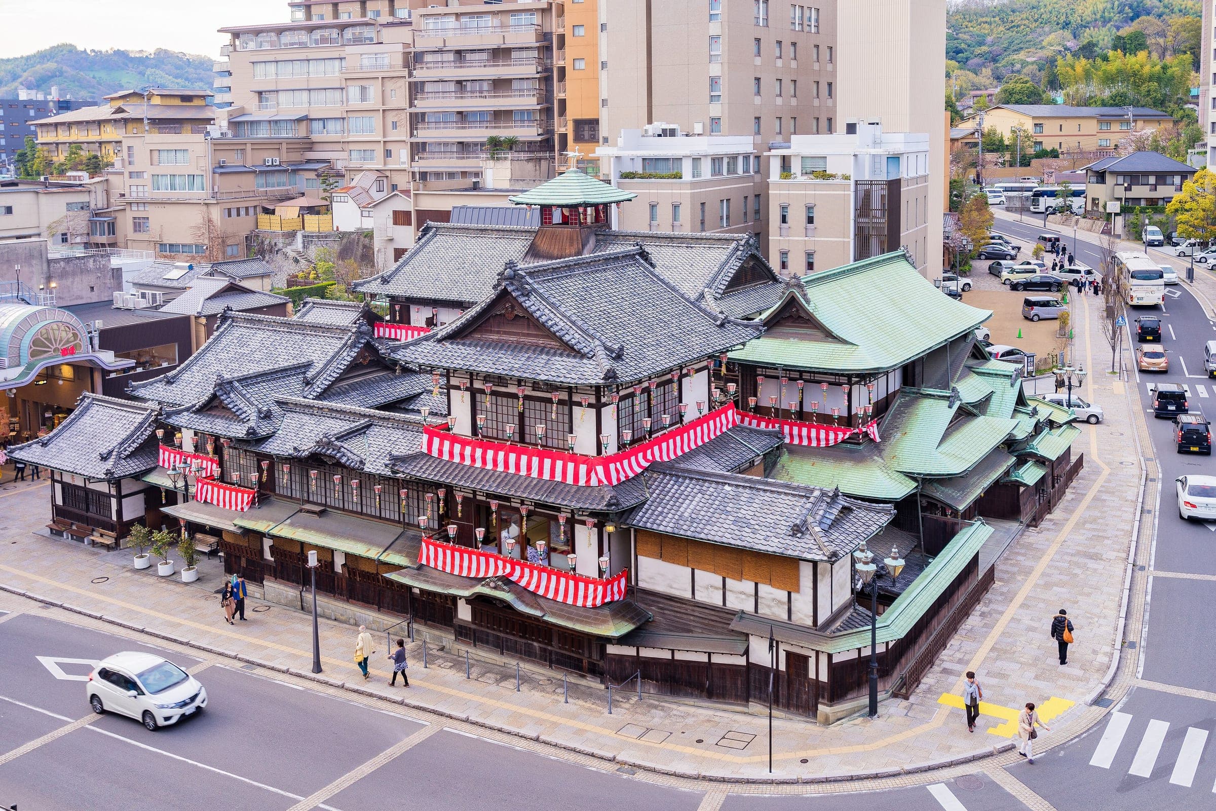 Dogo Onsen Honkan's tiled roofs and red-and-white bunting sit at a street corner in Matsuyama.