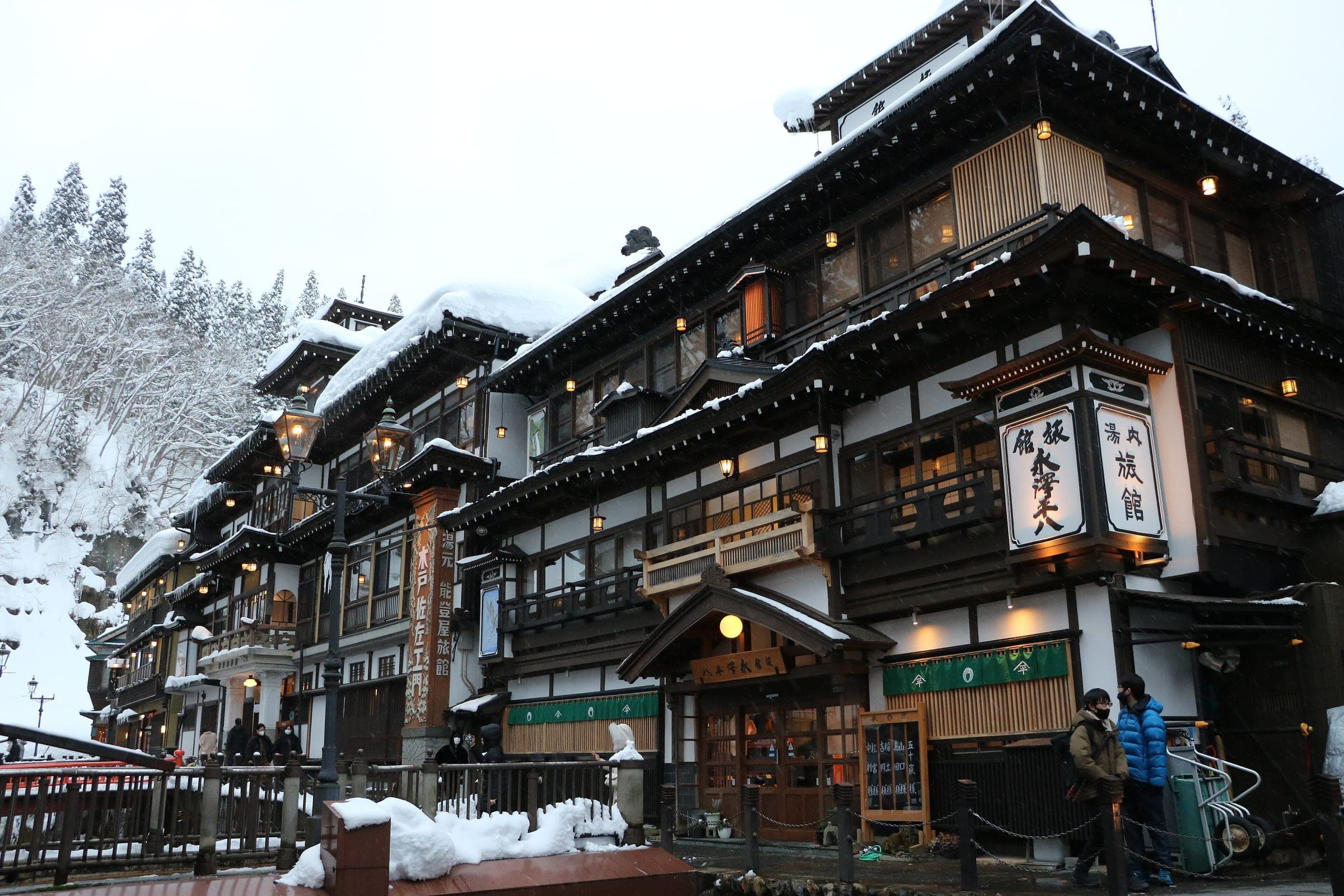Snow lies on the tiered wooden facade of Notoya Ryokan beside the river at Ginzan Onsen.
