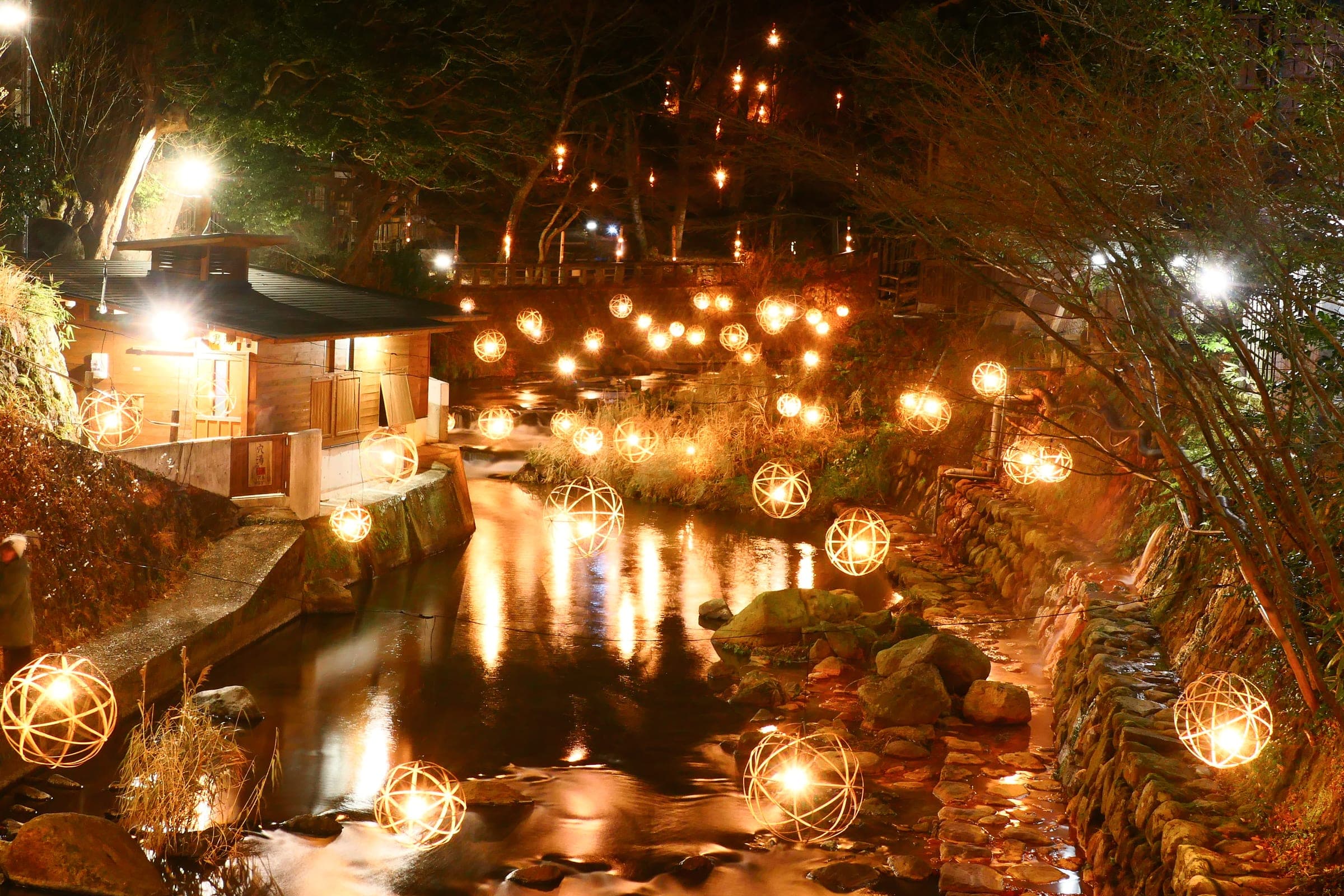Bamboo lanterns glow along the Tanoharu River through Kurokawa Onsen on a winter night.