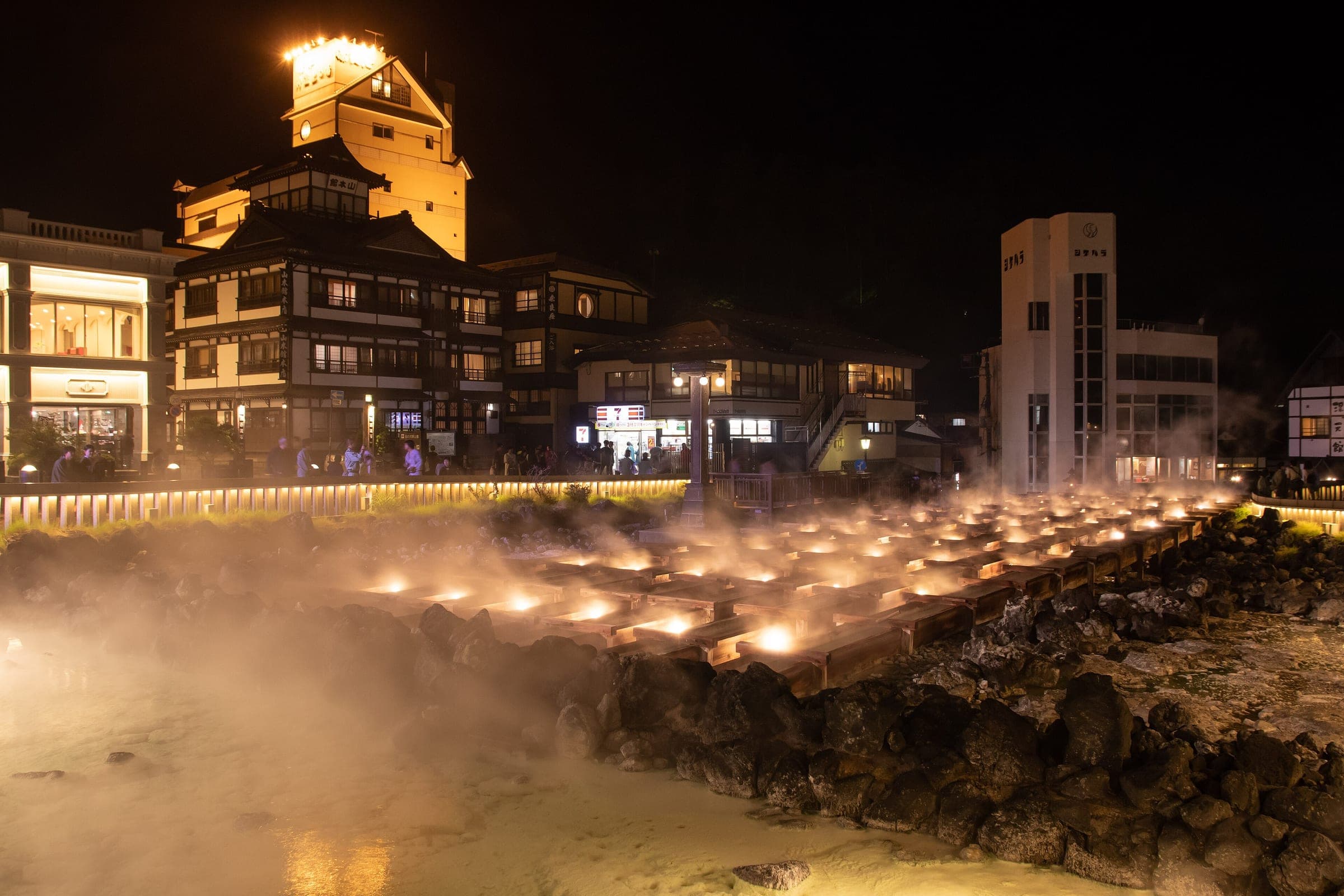 Lit wooden channels steam across the Yubatake in Kusatsu Onsen at night