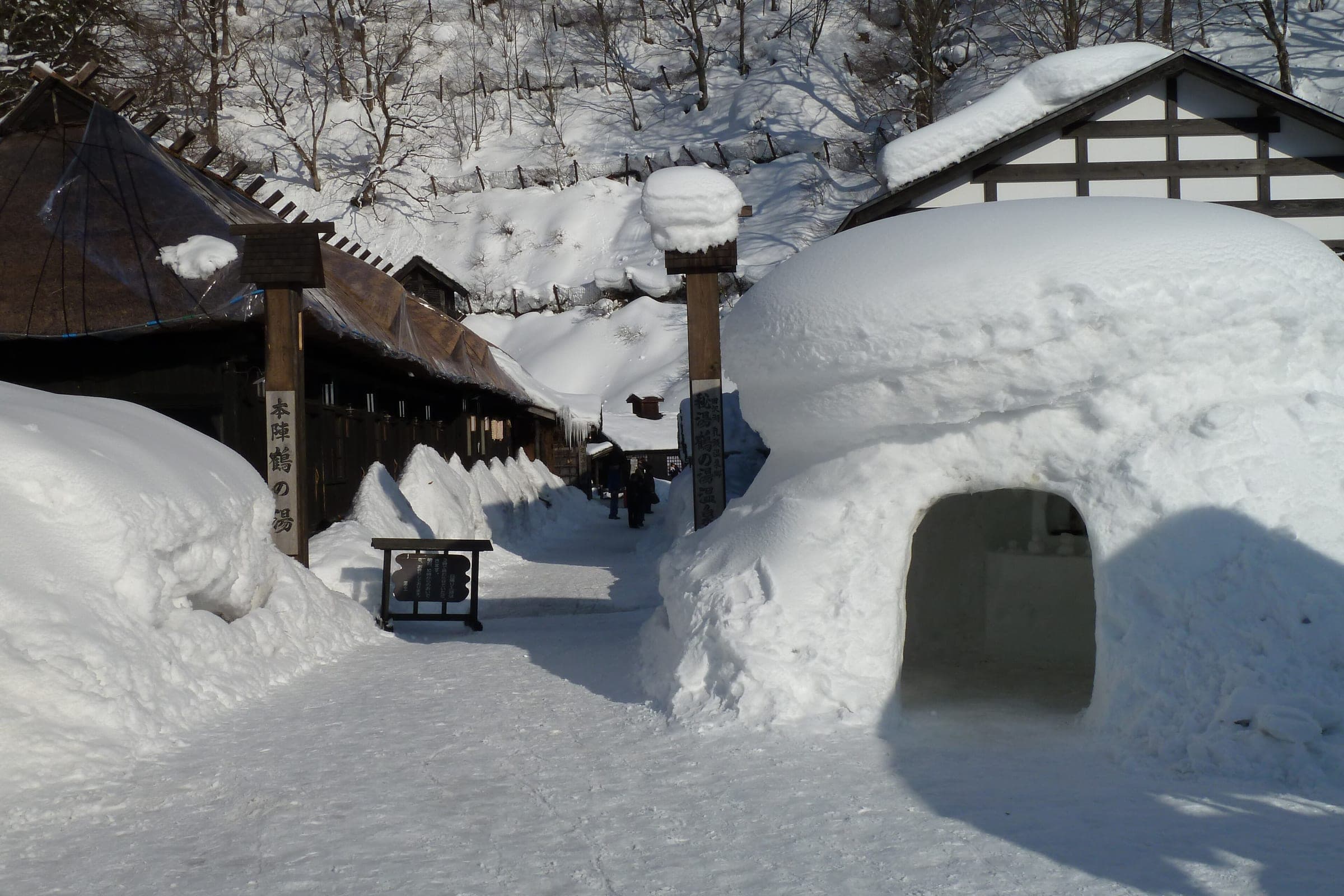 Deep snow banks and a snow hut line the lane past the thatched lodgings of Tsurunoyu Onsen.