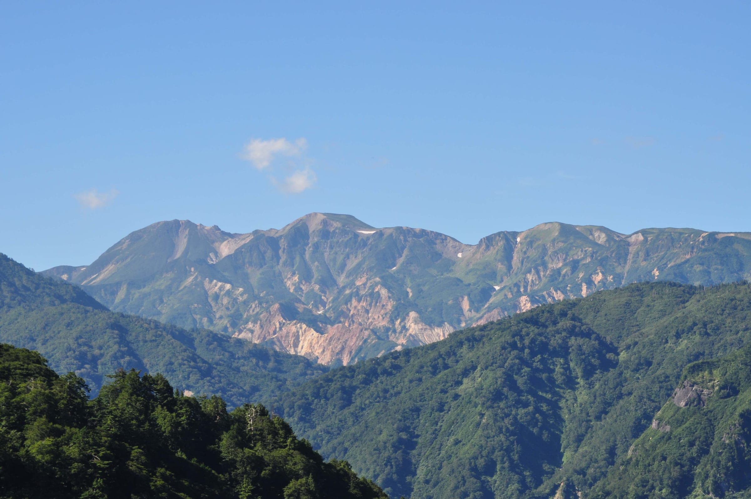Mount Haku's bare upper ridges rise above green forested slopes on a clear summer day