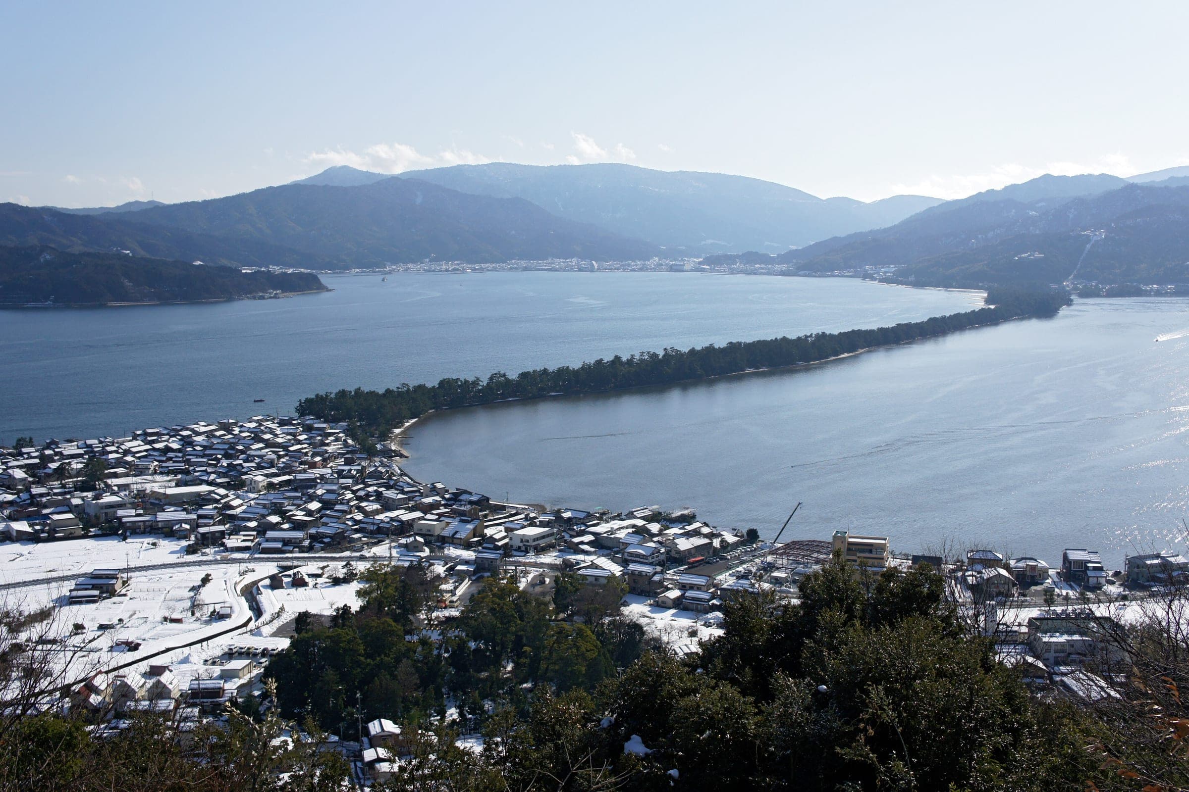 Snow dusts the roofs of Miyazu below the pine-covered sandbar of Amanohashidate in January