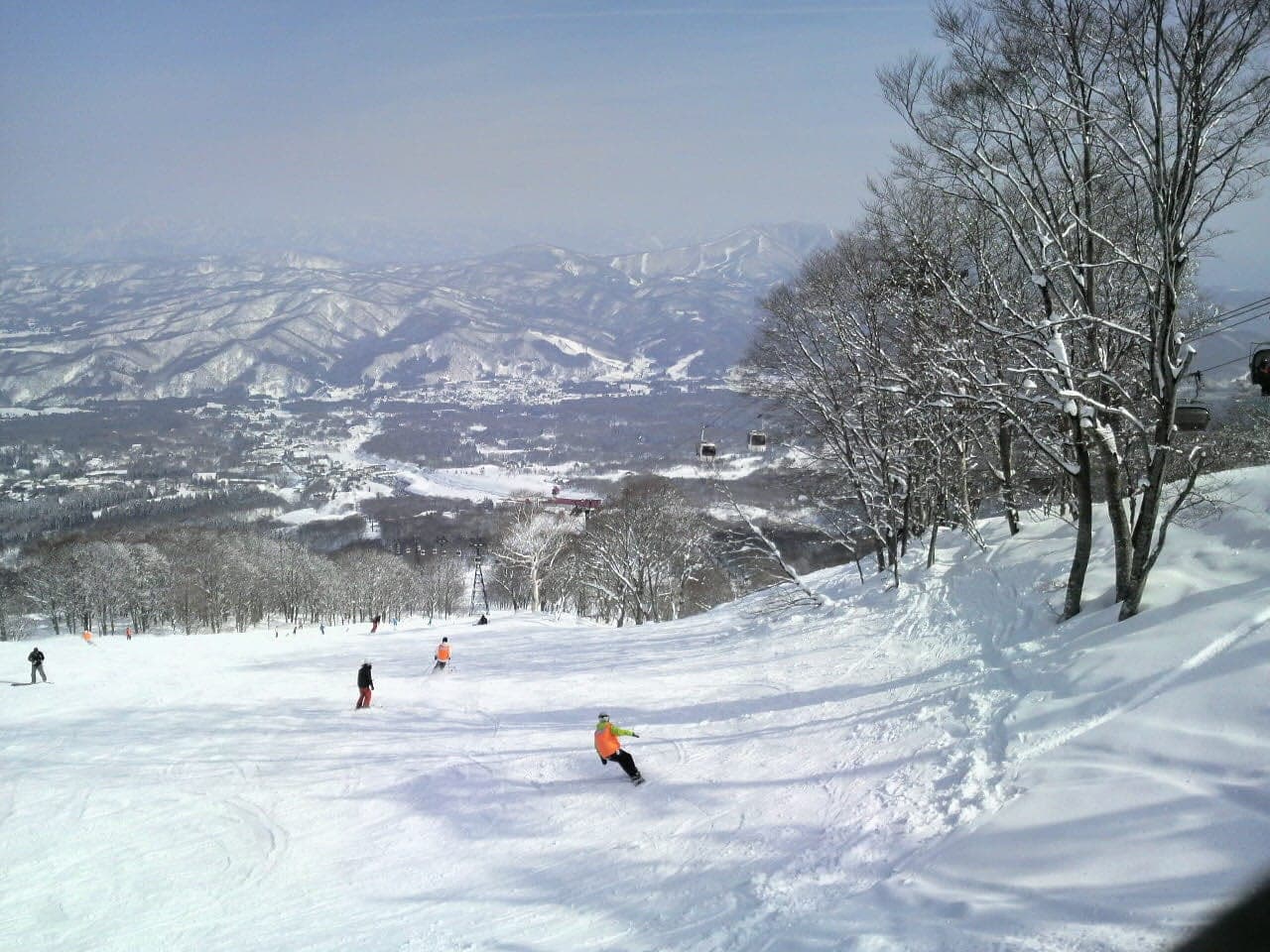 A snowboarder rides a sunny run at Akakura Kanko above the wide Takada plain