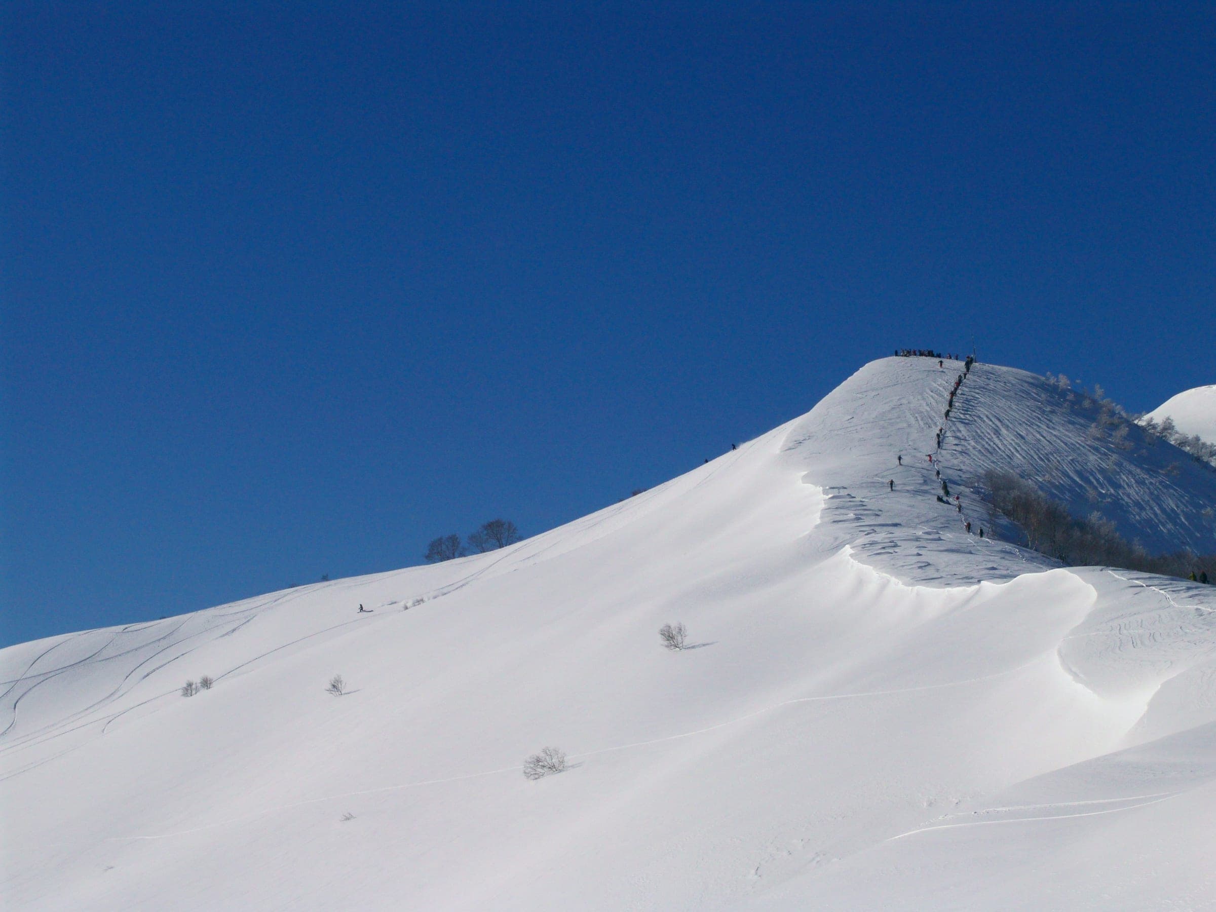 Riders bootpack up the wind-sculpted snow ridge of Mount Ohkenashi above Arai in January