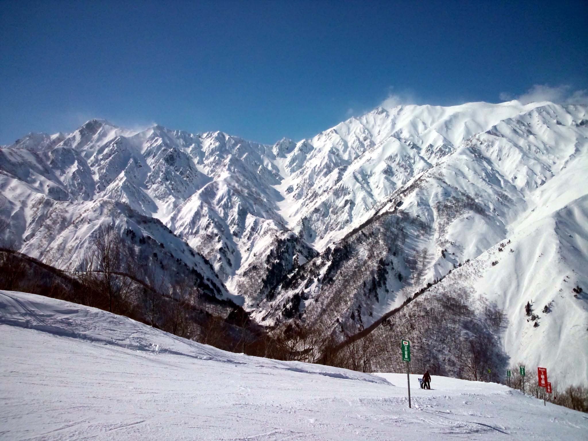 The snow-covered Hakuba range rises behind a groomed run at Hakuba47