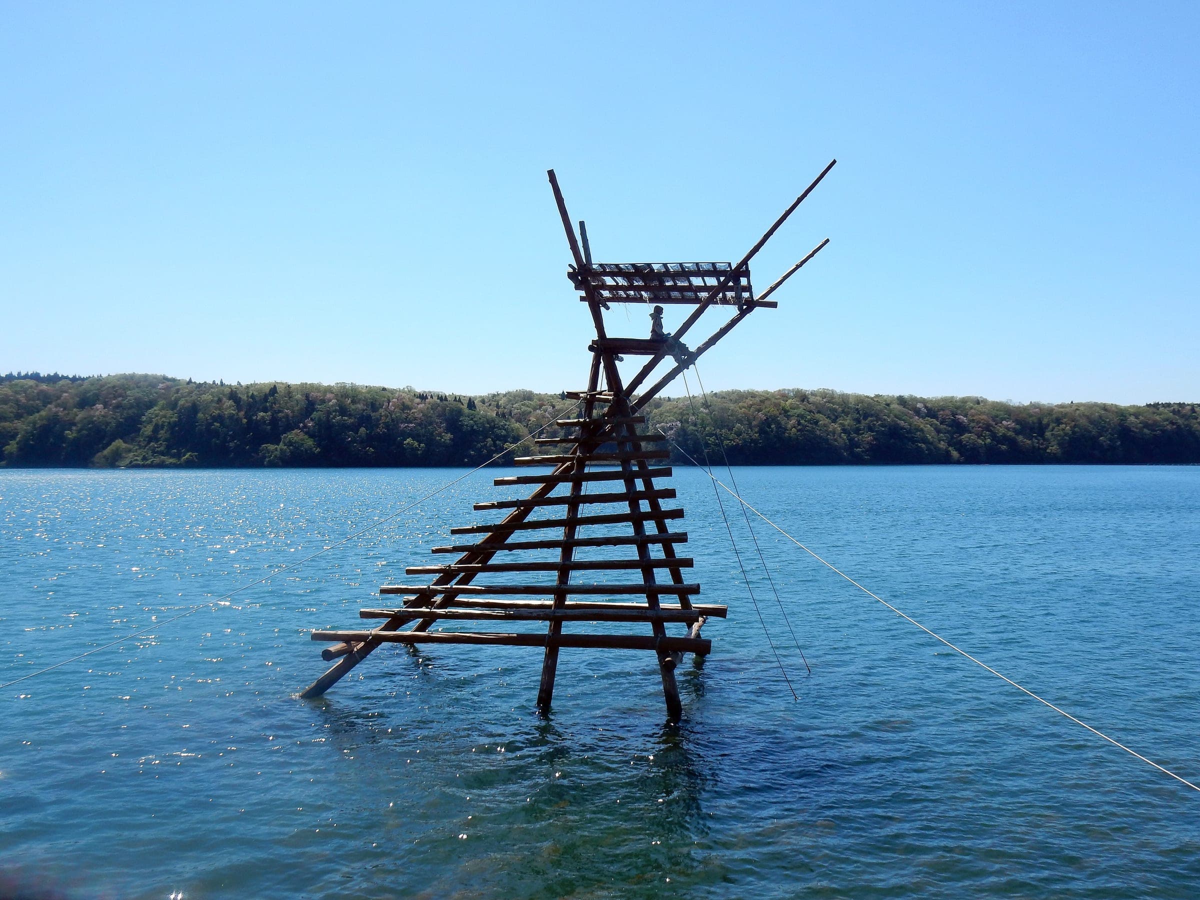 A wooden Boramachi Yagura fishing lookout stands in the calm blue water of Anamizu Bay in May